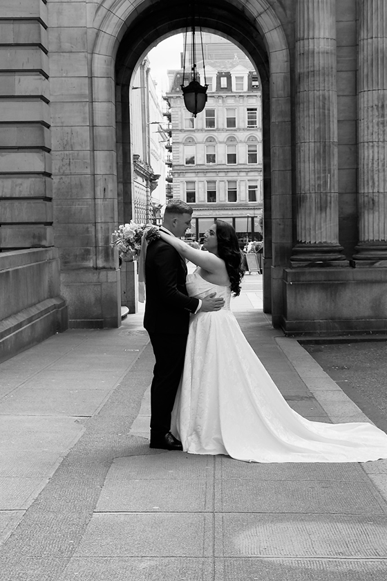 Black and white image of a bride and groom in front of arch outside City Chambers in Glasgow City Centre after getting married, image taken by wedding content creator, Content by Gail